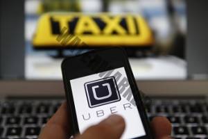 An illustration picture shows the logo of car-sharing service app Uber on a smartphone next to the picture of an official German taxi sign